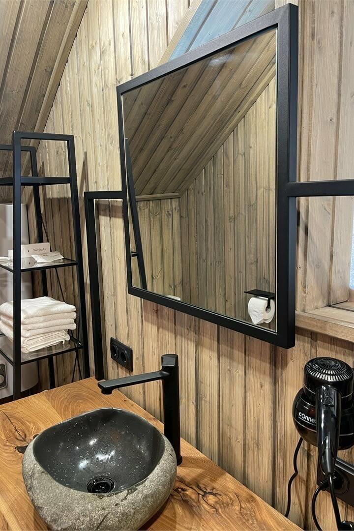 Ванная комната с каменной раковиной и чёрным зеркалом в раме.