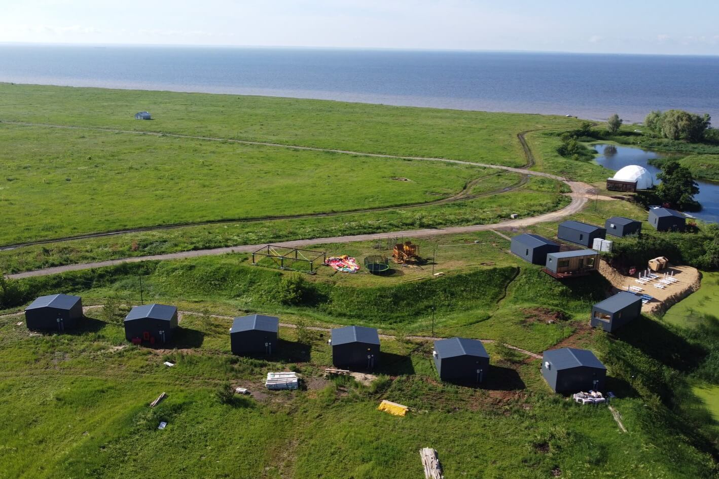 Ряд чёрных глэмпингов на зелёном склоне у моря.