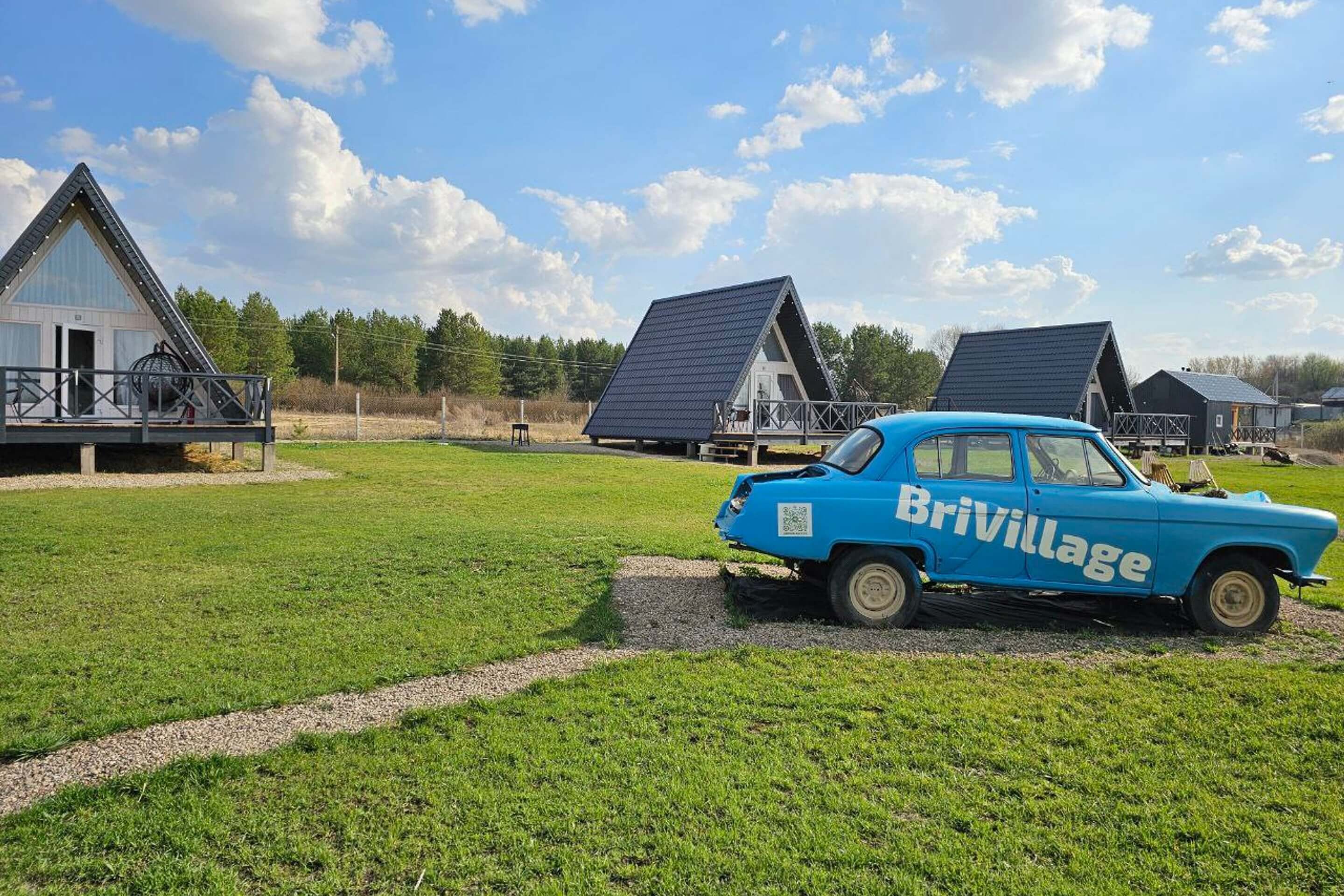 Синий автомобиль "BriVillage" на территории глэмпинга.