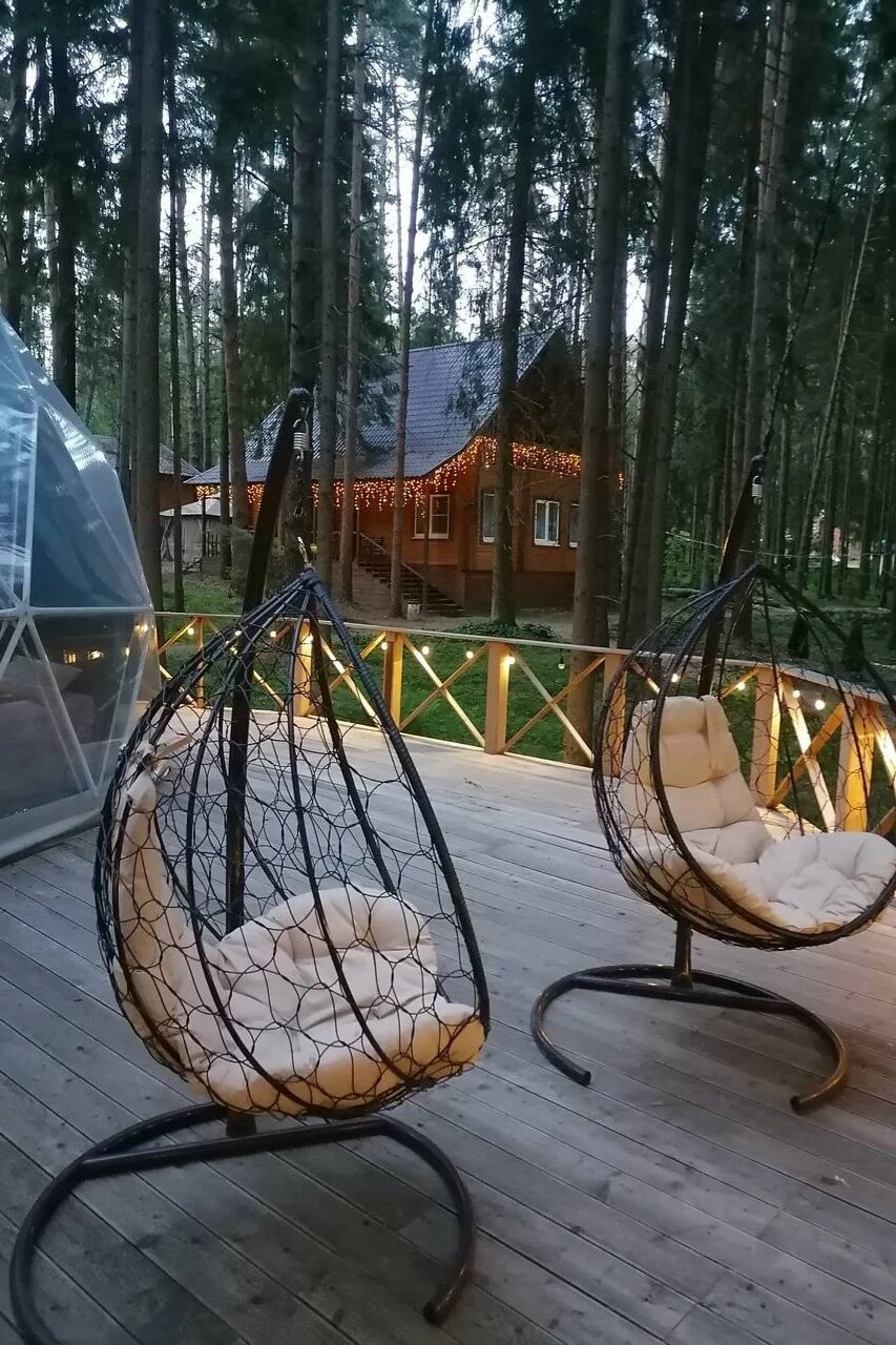 На деревянной террасе среди сосен подвесные кресла-коконы с подушками.