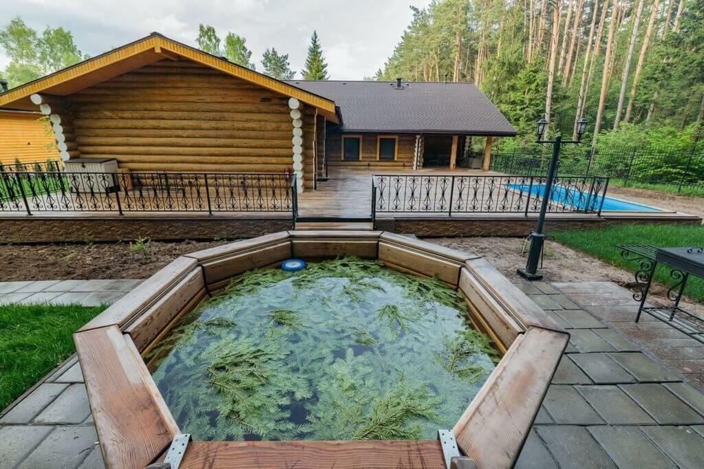 Деревянный сруб и главное здание у лесного озера с купелью.