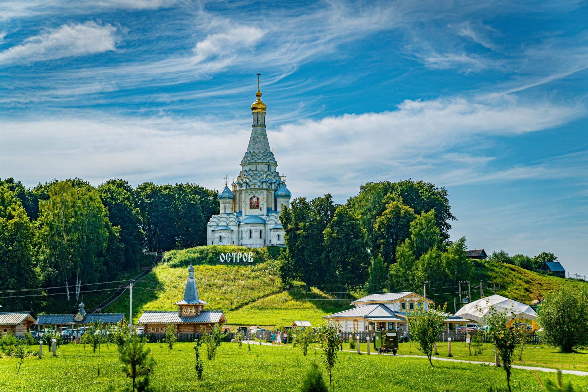 Церковь с золотым куполом на холме среди зелени.
