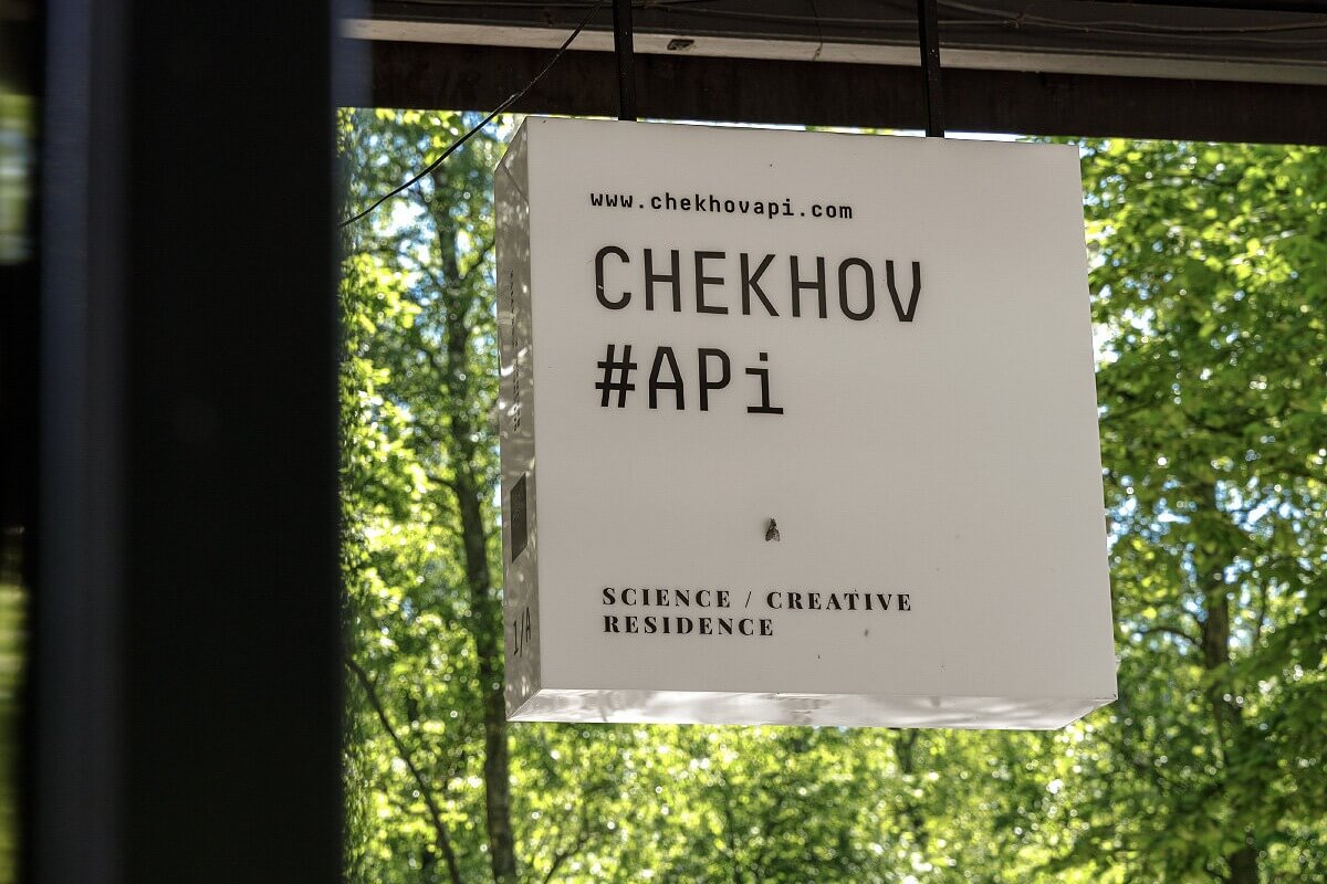 Вывеска научно-творческой резиденции Chekhov API среди зелени.