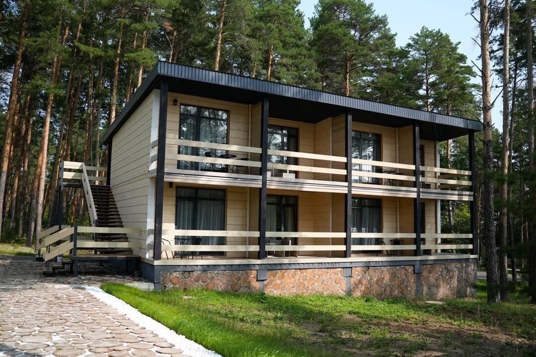 Двухэтажный каркасный дом с террасой среди сосен.