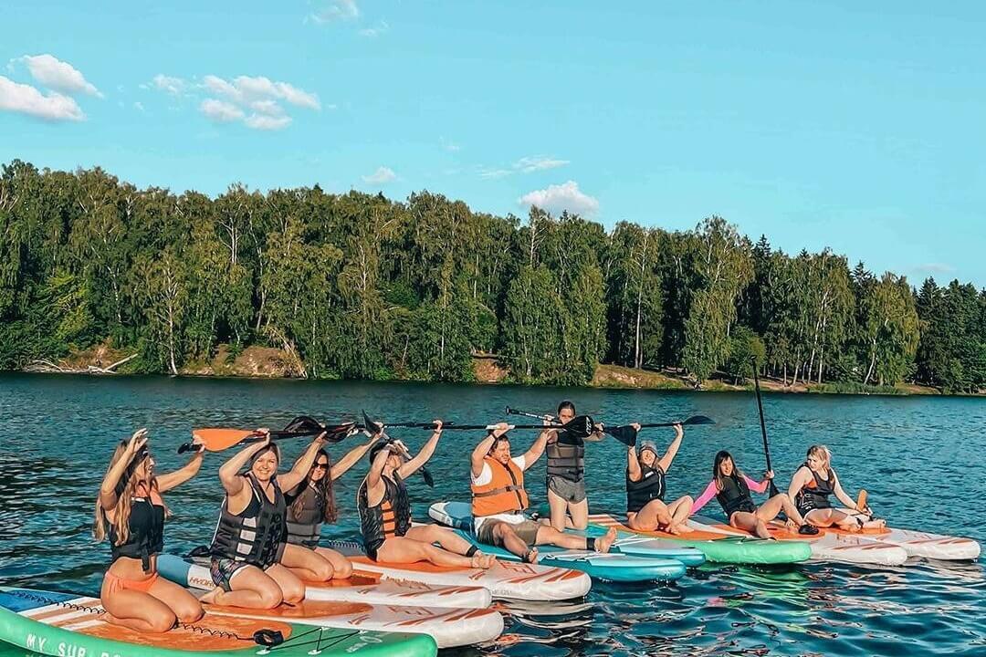 Групповое SUP-занятие на озере у лесного берега.