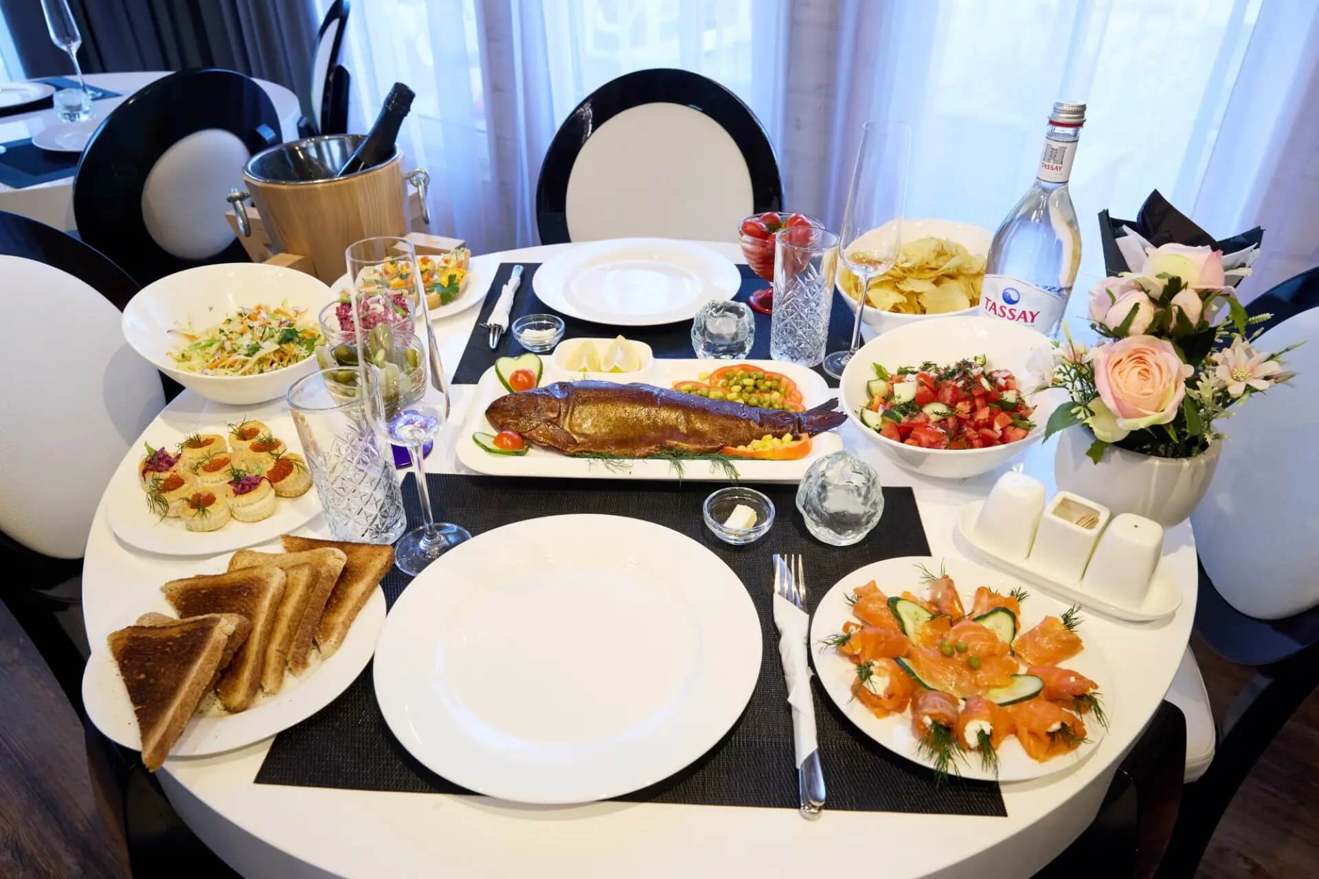 Праздничная сервировка обеда с рыбой и овощами на круглом столе.
