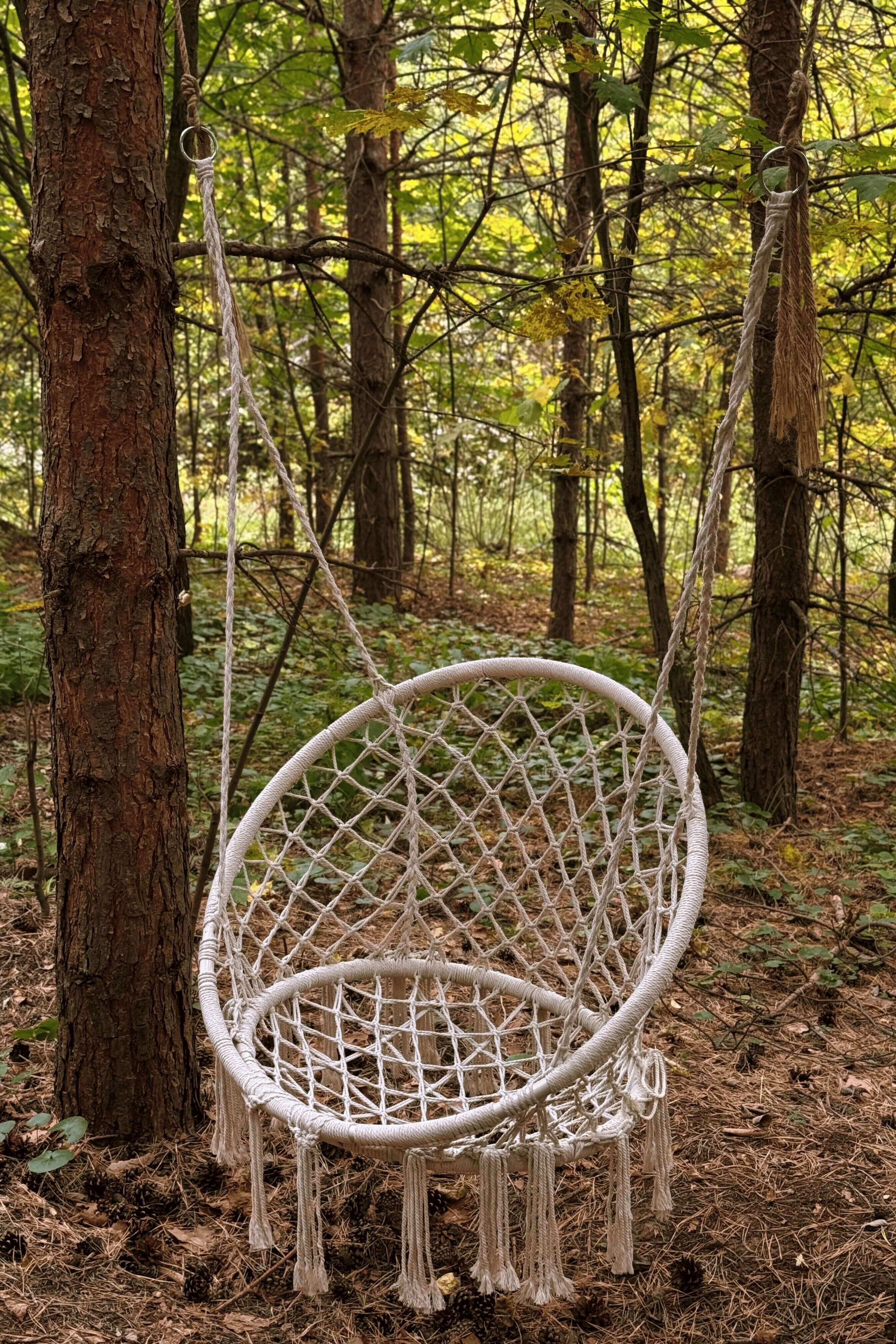 Подвесное кресло-качели из макраме среди лесных деревьев.