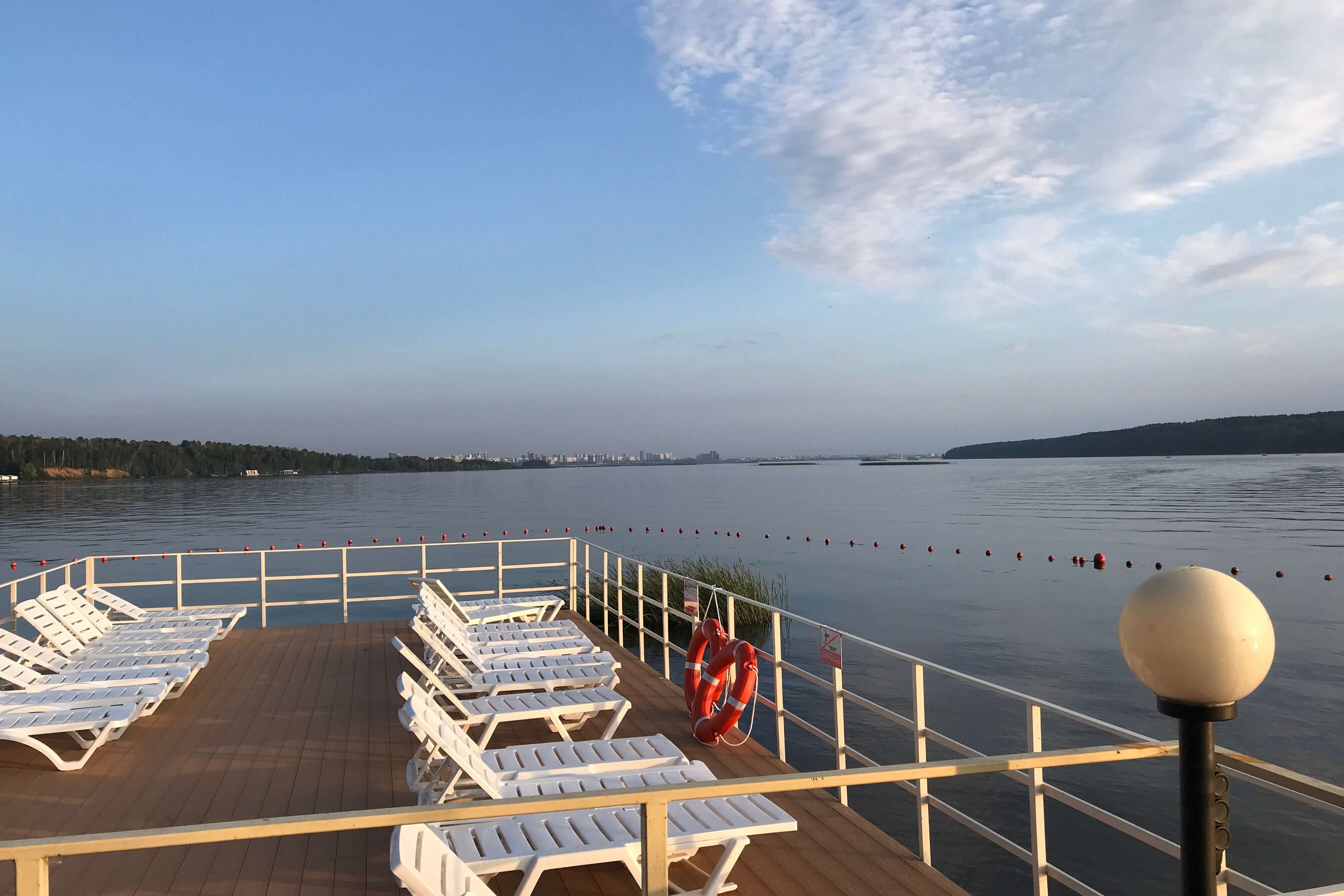 Деревянная палуба с лежаками на берегу озера.