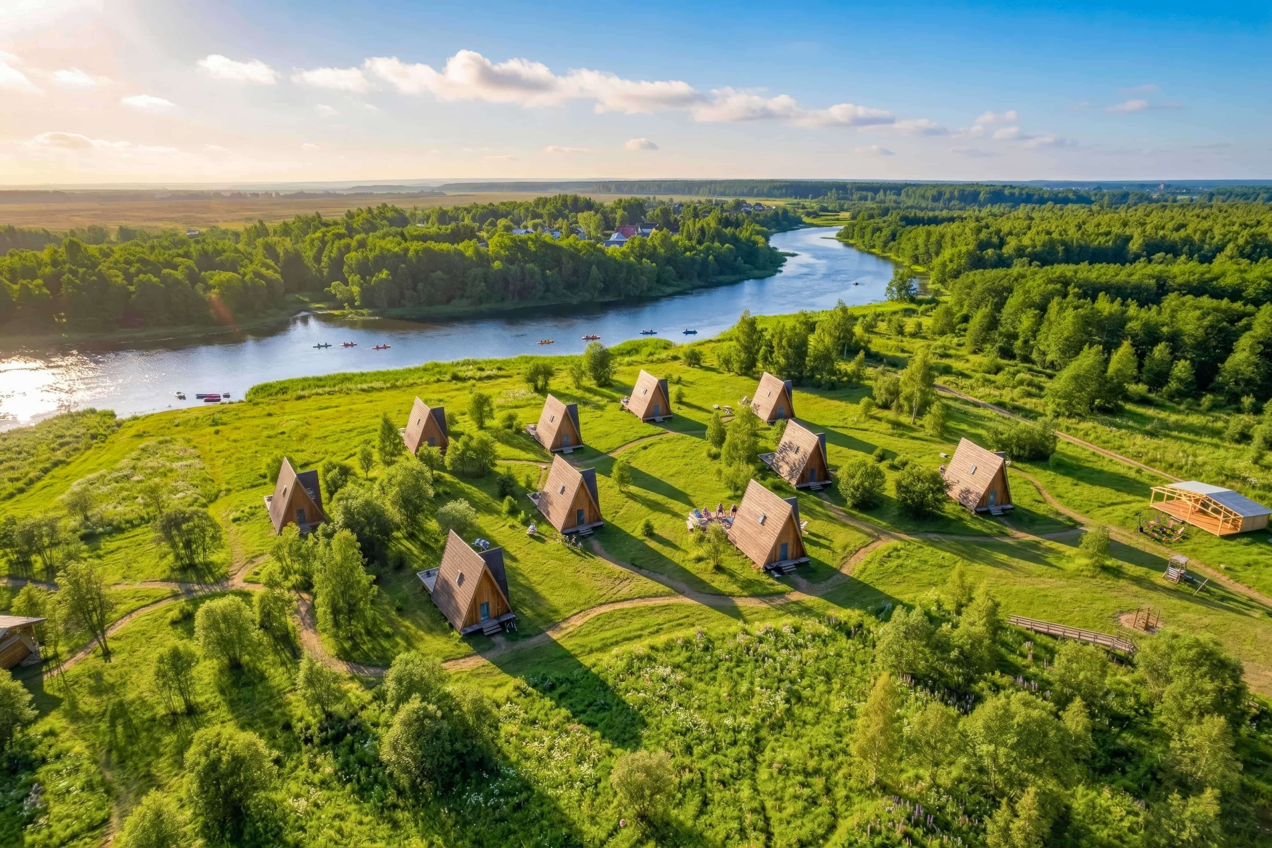 # Alt-текст для фотографии:

А-образные срубы на зеленом лугу у реки.