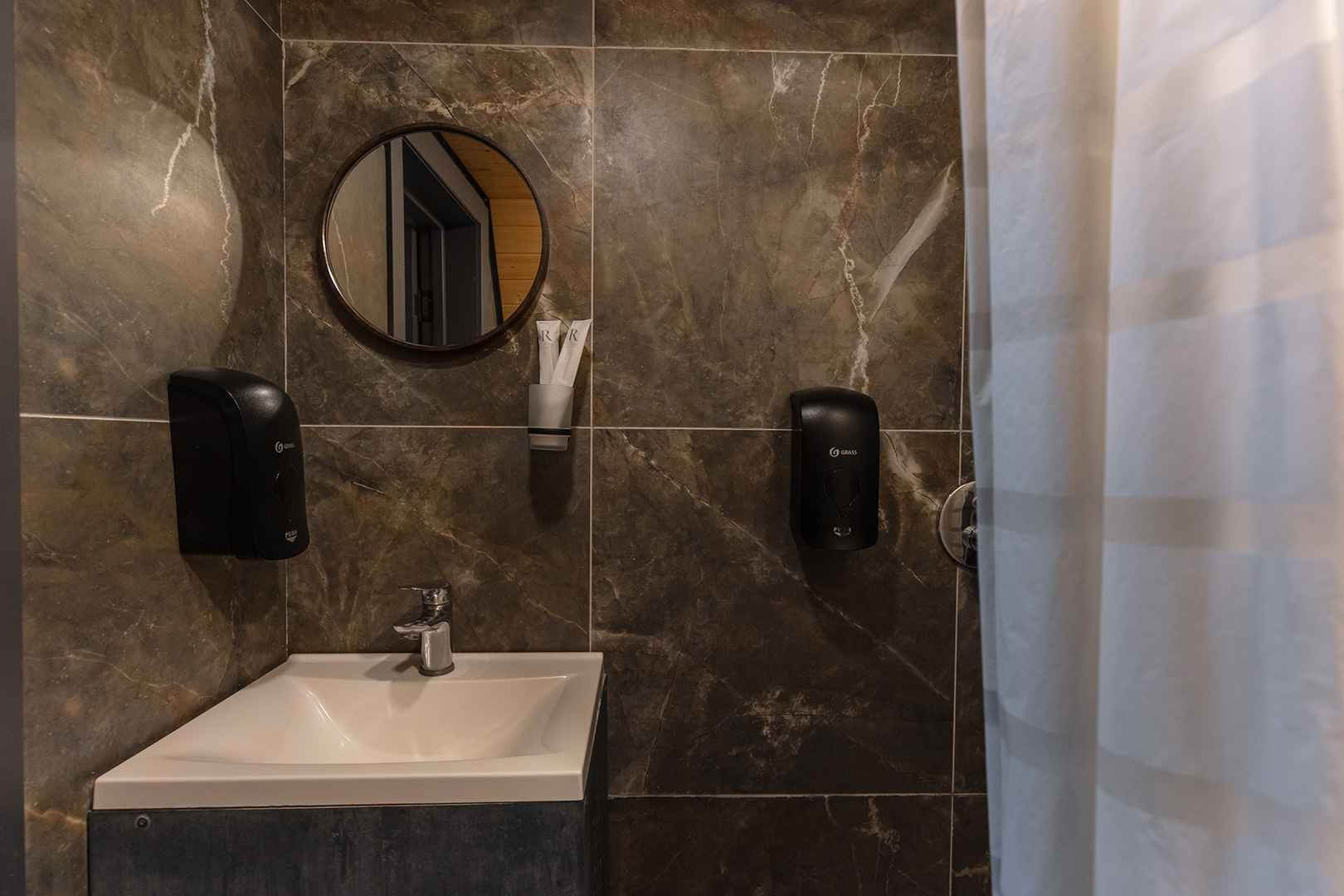 Ванная комната с мраморной плиткой и круглым зеркалом.