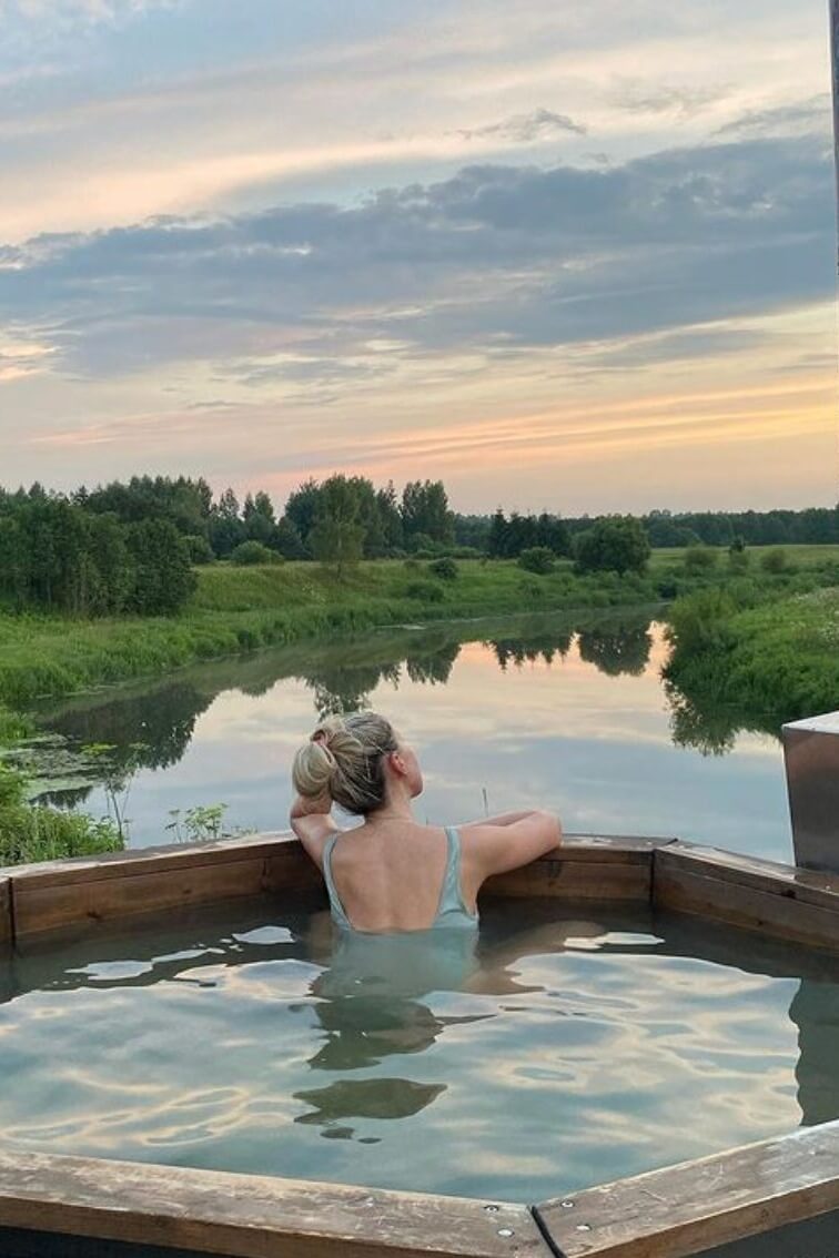 # Alt-текст для фото:

Гостья в открытой купели с видом на реку и лес на закате.