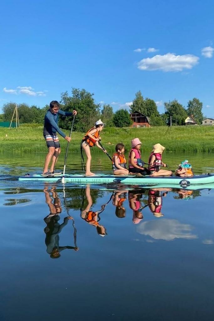 Семья на SUP-доске на спокойной реке среди зелени.
