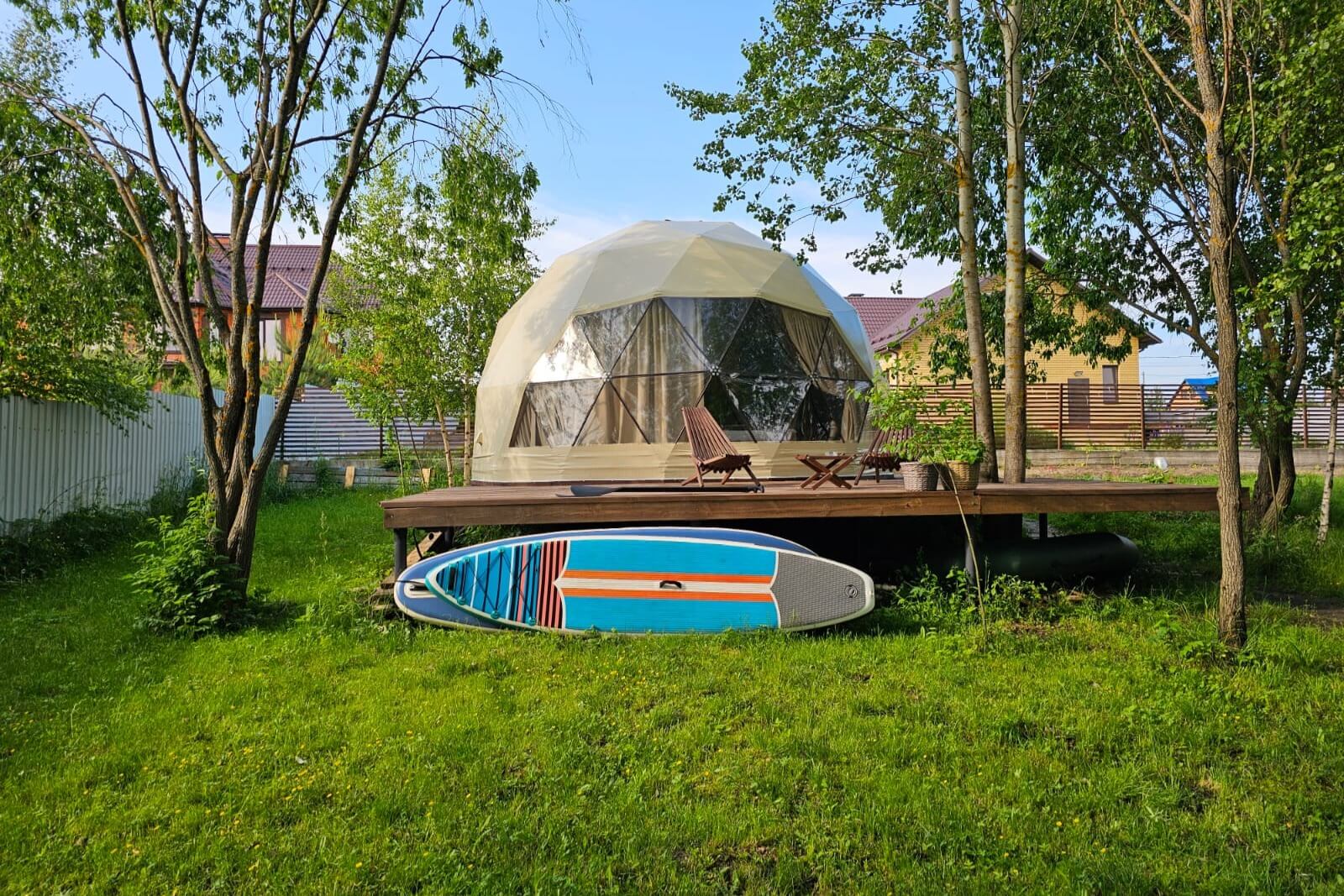 Купольная палатка на платформе среди деревьев с сёрфбордом.